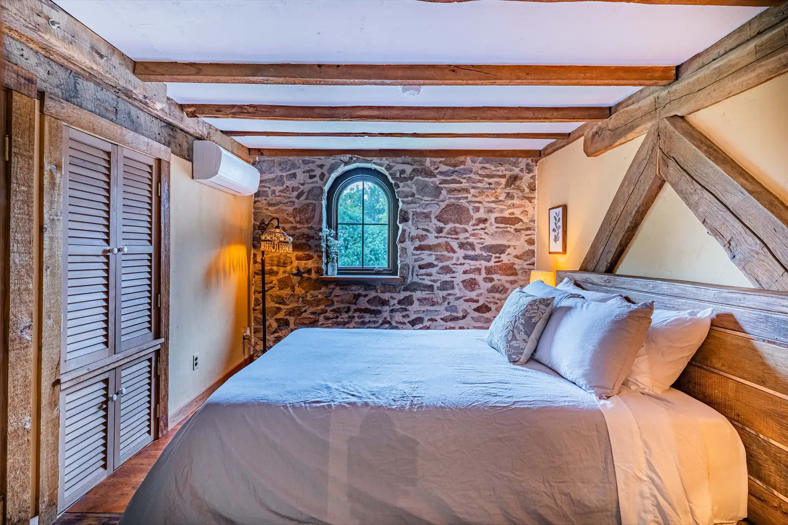 Bedroom with queen bed, arched stone window, and hand-hewn timber beams