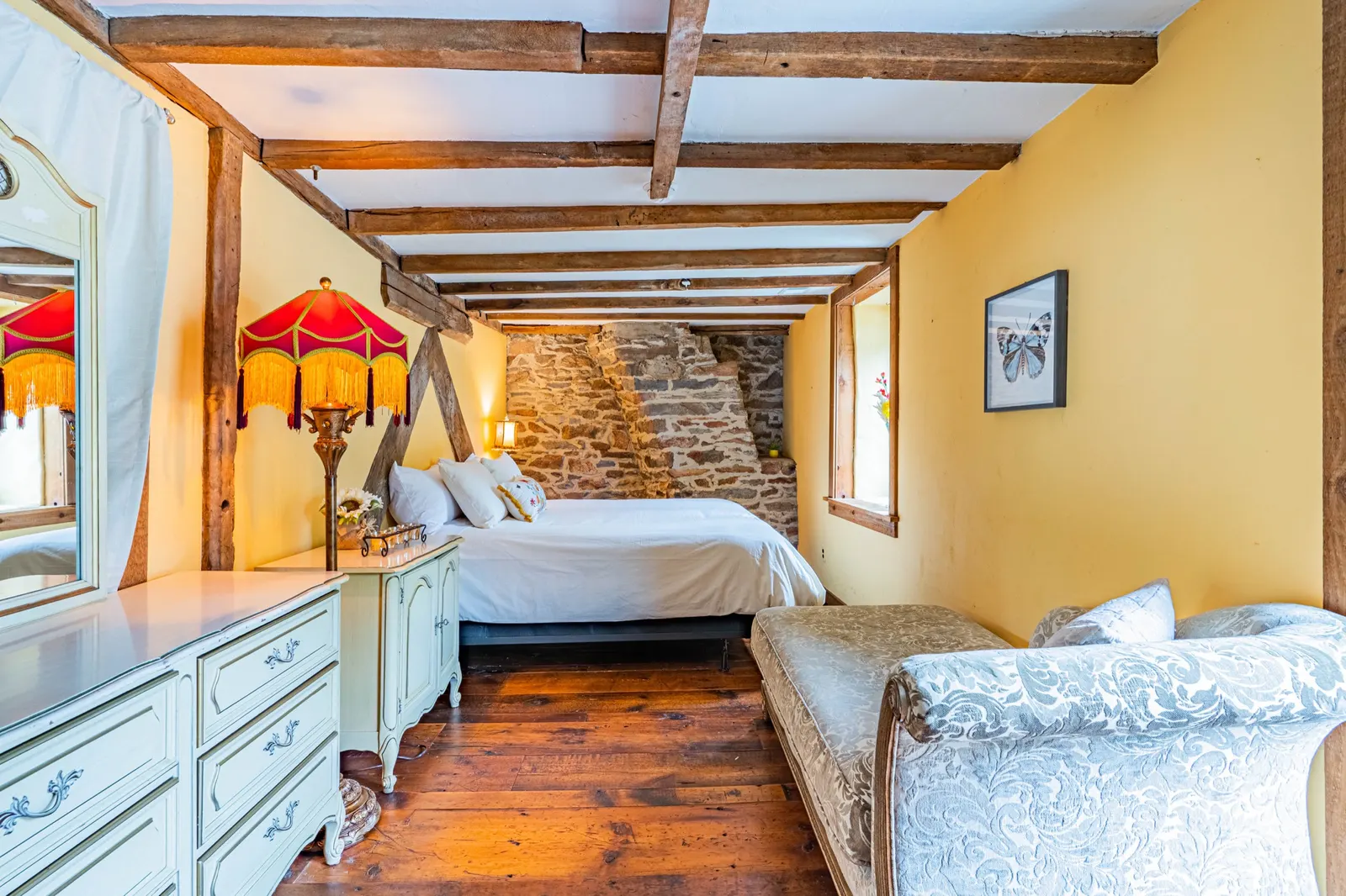 Bedroom with vintage red lamp, stone accent wall, chaise lounge, and dresser