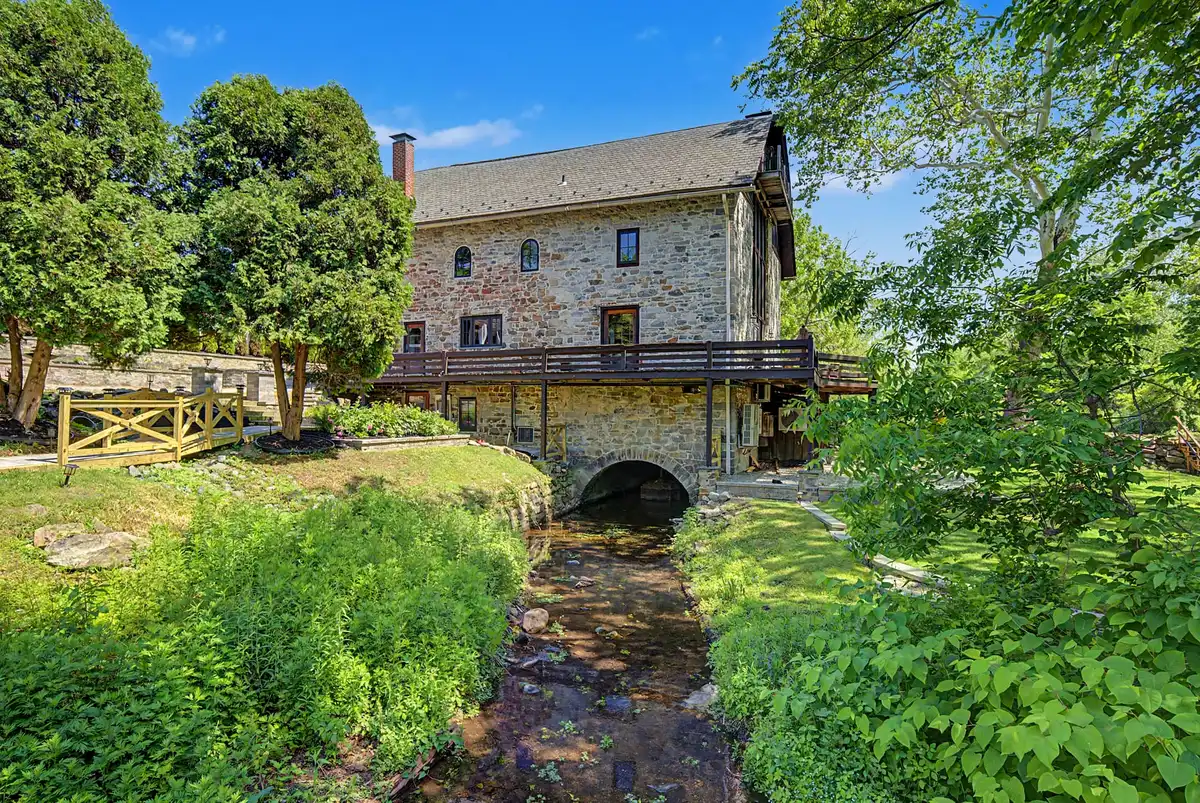Stream flowing out of the arched tailrace opening beneath the stone mill, wraparound deck above