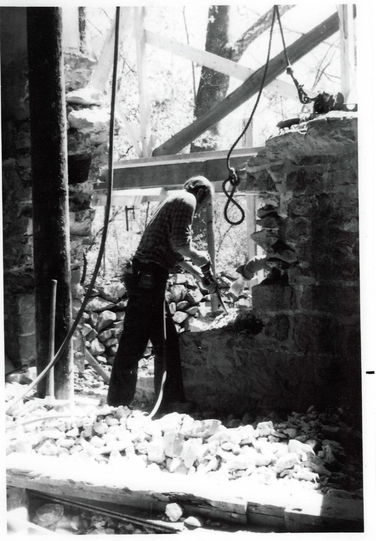 Donald Cole working a jackhammer against the mill's stone wall, rubble heaped at his feet