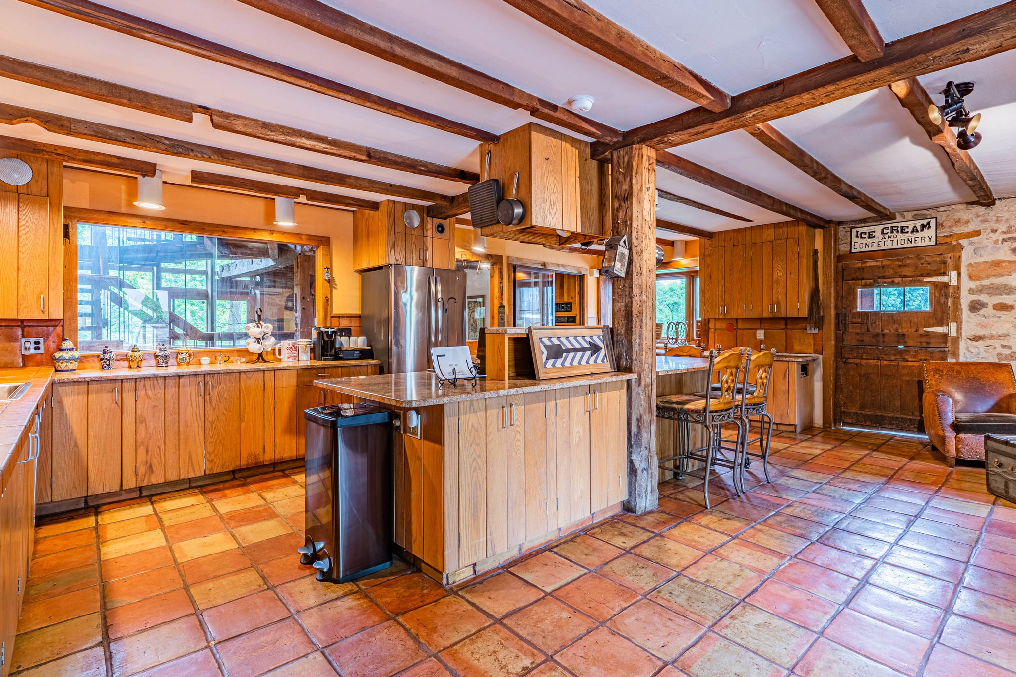 Spacious kitchen with wooden cabinetry, terra cotta tile floor, and exposed beams