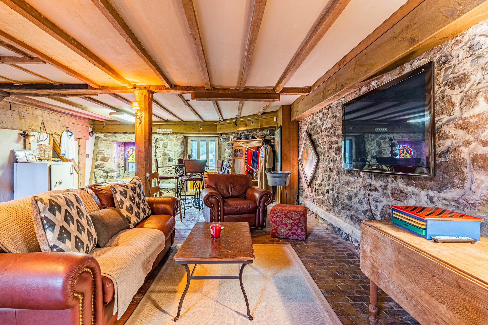 Lower-level lounge with leather sofas, large TV, stone wall, and brick floor