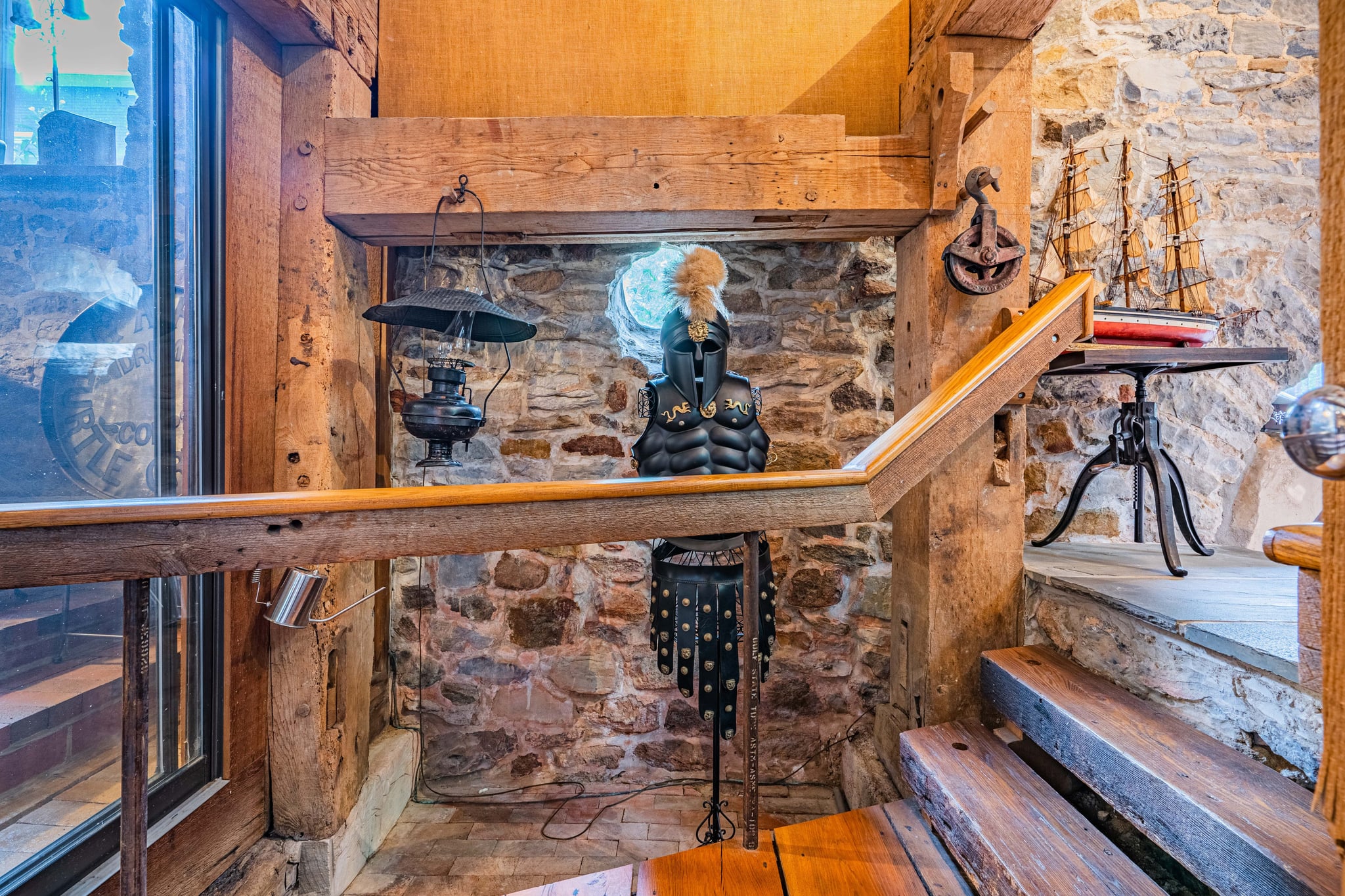 Stairwell landing with medieval armor display, stone walls, and ship model