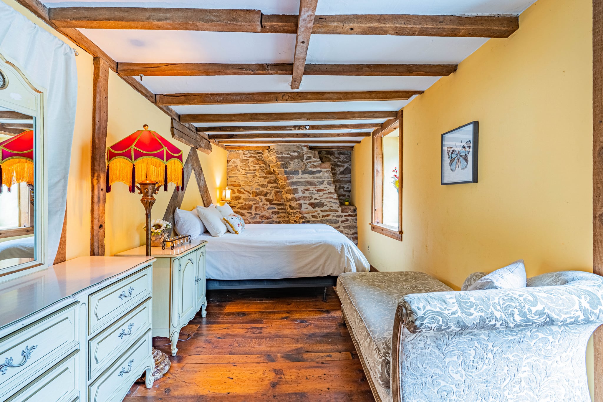 Bedroom with vintage red lamp, stone accent wall, chaise lounge, and dresser