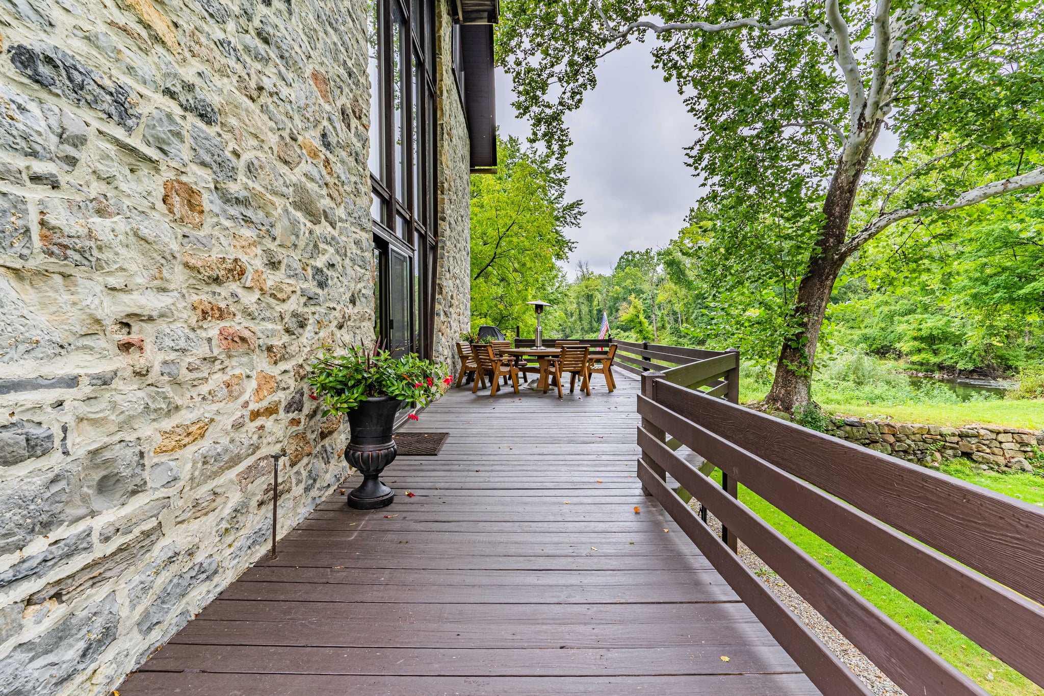Wraparound deck along the original stone wall with potted flowers and river views